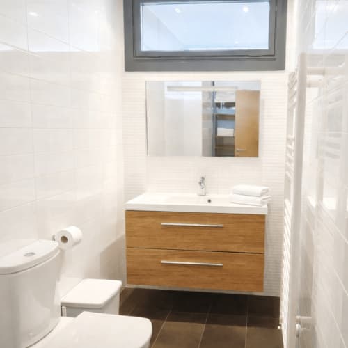Baño moderno en apartamento Holibai Baiona con vanidad de madera, azulejos blancos tipo metro, gabinete espejo y tragaluz