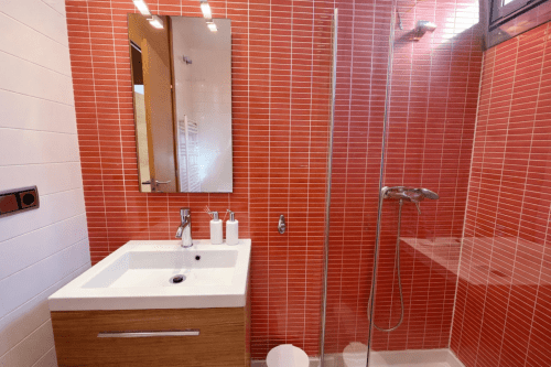 Baño moderno con paredes de azulejos rojos, lavabo blanco con tocador de madera, espejo y ducha con cabina de vidrio en Holibai Beiramar