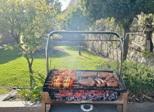 Parrilla de jardín al aire libre en la casita Holibai de Baiona con carnes y verduras cocinándose en el entorno del jardín