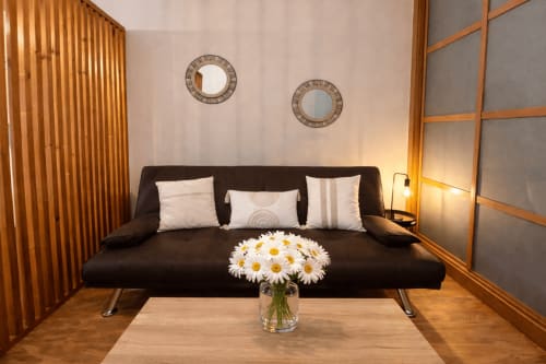 Sala moderna con sofá negro, cojines blancos y margaritas blancas en jarrón de cristal en apartamento Holibai cerca de playa Baiona