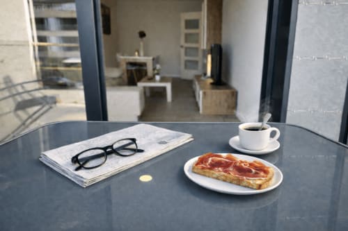 Mesa de desayuno en el apartamento Bon Xeito de Baiona con café, pastel, periódico y vasos sobre la mesa de la terraza