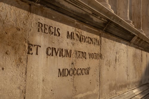 Latin inscription on stone wall at Le Prieuré Notre-Dame, Montfrin, FR - historic engraved text reading 'REGIS MUNIFICENTIA
