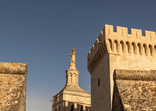 Golden stone chapel with cross-topped spire at Le Prieuré Notre-Dame in Montfrin, France, viewed through medieval