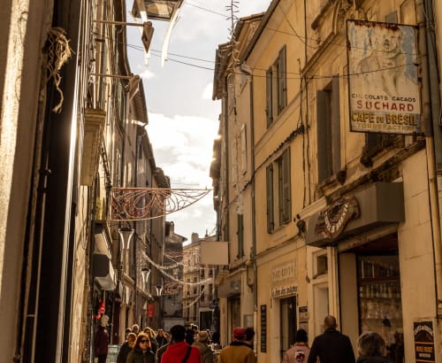 Historic narrow French street in Montfrin with aged buildings, vintage signs, and tourists walking through charming old town