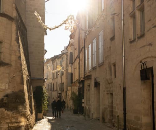 Golden-lit medieval street in Montfrin, France with stone buildings and festive garland decorations