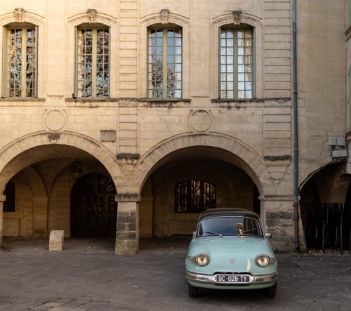 Vintage light blue car parked in courtyard of Le Prieuré Notre-Dame, a French BnB in Montfrin with arched stone architecture