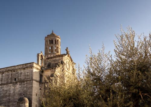 Historic stone church tower with bell tower at Le Prieuré Notre-Dame in Montfrin, France, surrounded by olive trees