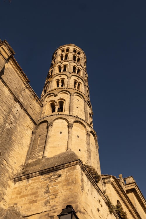Medieval bell tower of Le Prieuré Notre-Dame in Montfrin, France, illuminated against blue sky
