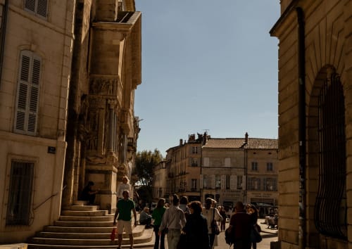 Charming narrow street in Montfrin with historic stone buildings, pedestrians, and warm Mediterranean architecture near Le