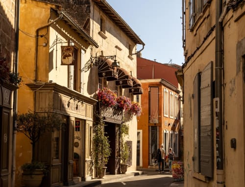 Charming medieval street at Le Prieuré Notre-Dame in Montfrin, France with historic buildings and flowering window boxes