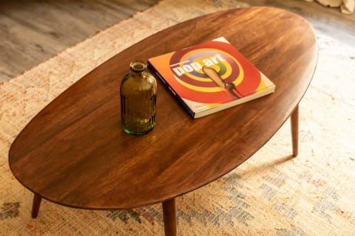 Wooden oval coffee table with dark glass bottle and red art book, styled in Le Prieuré Notre-Dame guesthouse in Montfrin,