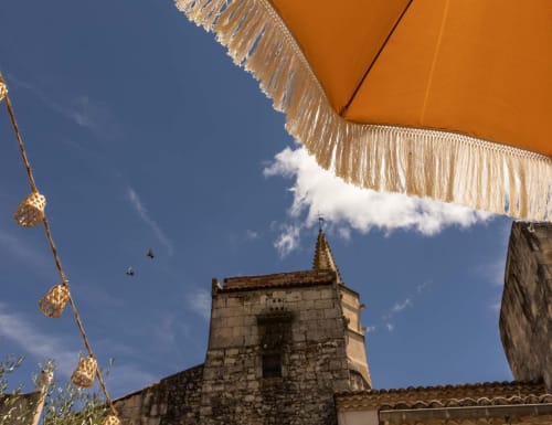 Orange parasol with golden fringe overlooking stone church tower at Le Prieuré Notre-Dame in Montfrin, France