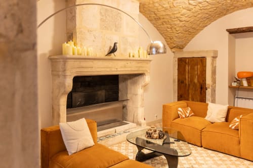 Elegant living room at Le Prieuré Notre-Dame with stone fireplace, orange seating, and arched ceiling in Montfrin