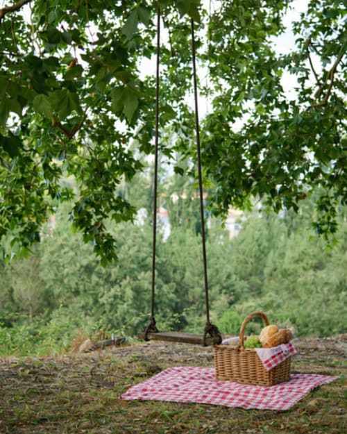 Rustic swing under leafy trees with picnic basket and red checkered blanket at Quinta da Alcaidaria-Mór in Ourém-Fátima,