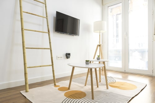 Sala de estar moderna en Málaga con escalera de bambú, muebles de madera, TV mural, lámpara de pie y alfombra geométrica