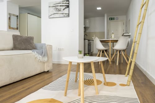 Moderna sala de estar en Málaga con sofá crema, mesa de comedor de madera, sillas blancas y detalles de bambú