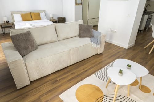 Estudio moderno en Ab Be Apartments de Málaga con sofá beige, mesitas blancas, suelos de madera y zona de cocina