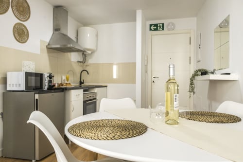Moderna zona de cocina-comedor en Apartamentos Ab Be, Málaga, con sillas blancas, mesa de comedor, cocina equipada y señal de salida
