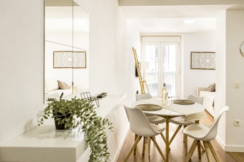 Comedor moderno en Ab Be Apartments Málaga con sillas blancas, mesa de madera, luz natural desde las puertas del balcón y vistas a la ciudad