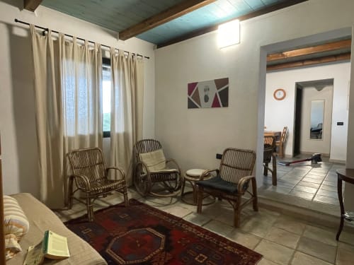 Bright cottage living room with wicker chairs, red rug, cream curtains, and sea views in Orosei villa