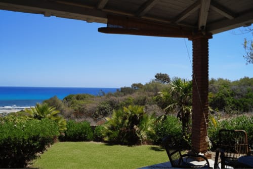 Veranda view of Mediterranean sea and coastal garden at Cottage Fuile Mare, Orosei villa with palm trees and lawn