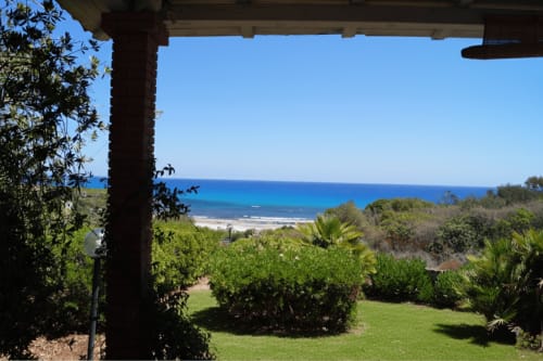 Veranda view of Orosei villa with manicured lawn, sea view, and Mediterranean coastline under blue sky