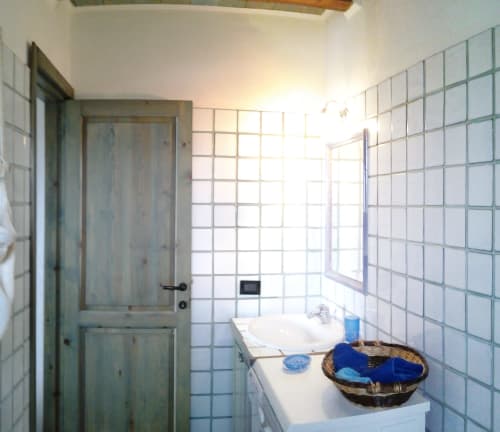 Bright bathroom with white tile walls, sink, and green wooden door in Orosei villa rental