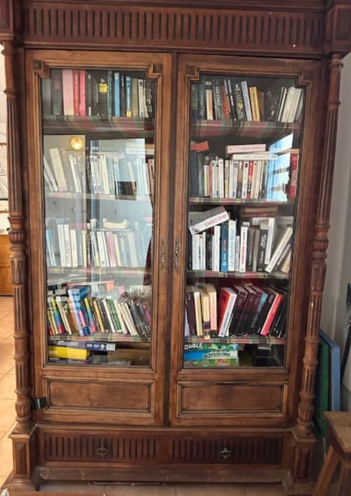 Libreria in legno con ante in vetro piena di libri e media all'hotel Les Créolines, Sainte-Luce