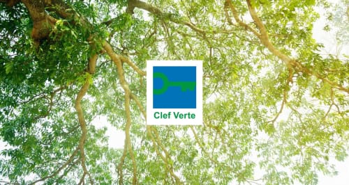 Logo de Clef Verte certificado ecológico exhibido sobre fondo de dosel de árboles en el Hôtel De La Fontaine en Niza