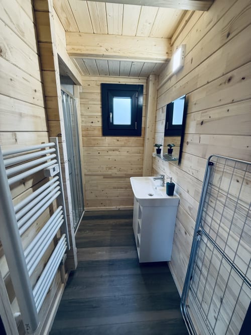 Salle de bain contemporaine en pavillon boisé avec lavabo, radiateur sèche-serviettes, miroir et sol foncé