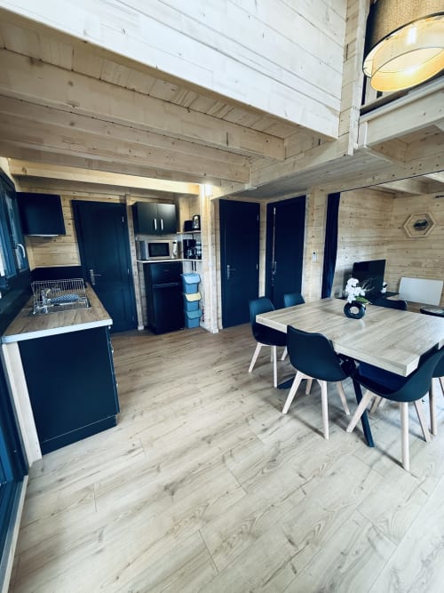 Intérieur de lodge moderne avec poutres en bois, table à manger, coin cuisine et portes bleu foncé aux Cabanes et lodges du Belvédère
