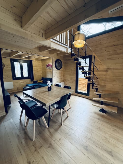 Salle à manger du lodge Belvédère avec chaises noires, table en bois, escalier spirale et puits de lumière