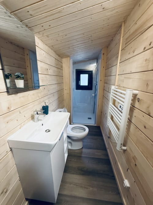 Salle de bain moderne en bois de la villa Lodge l'ORCHIDÉE avec lavabo blanc, toilettes, sèche-serviettes chauffant et sol foncé