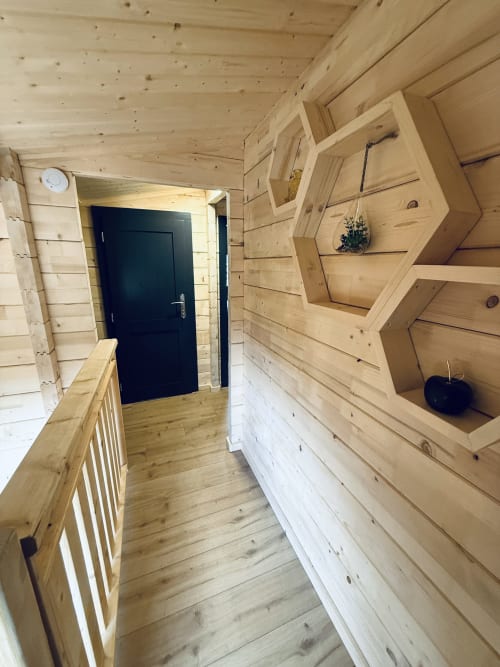 Intérieur d'un lodge en bois avec étagères de rangement hexagonales, parquet, porte bleu foncé et rampe