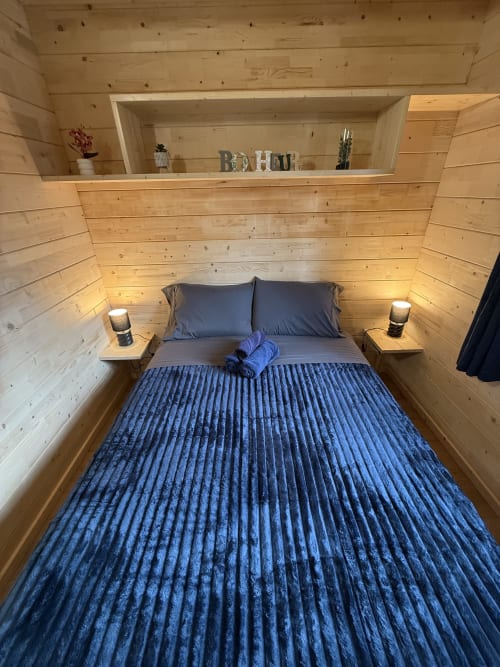 Chambre douillette en bois avec literie bleue, étagère intégrée et lampes de chevet aux Cabanes du Belvédère