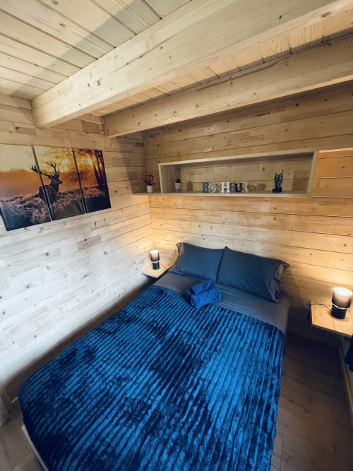 Chambre douillette en bois avec literie bleue, poutres apparentes, étagères et art animalier aux Cabanes et lodges du Belvédère