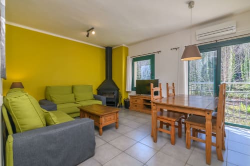 Bright living and dining area with lime green sofas, wooden table, fireplace, and mountain views at Rural Montseny apartment