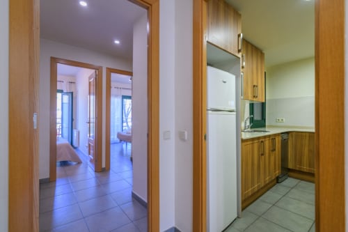 Kitchen and hallway of 2-bedroom apartment at Rural Montseny with wooden cabinetry, refrigerator, and tile flooring