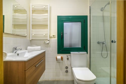 Modern bathroom in Rural Montseny apartment with wooden vanity, white tile, green-framed window, and glass shower enclosure