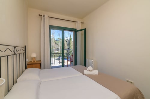 Bright bedroom with double bed, green balcony doors overlooking mountains in Rural Montseny apartment, Gualba