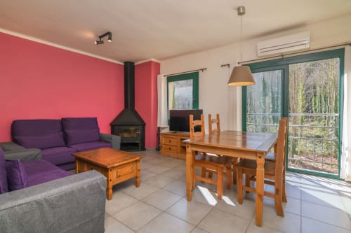 Open-plan living area in Rural Montseny apartment with purple sofa, wooden dining table, fireplace, and mountain views