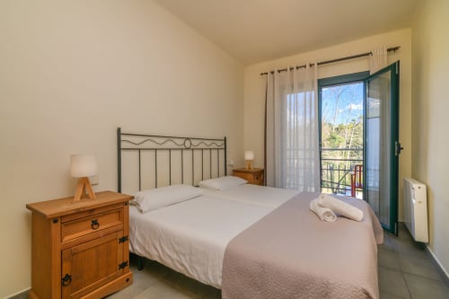 Bright bedroom in Rural Montseny apartment with metal bed, wooden nightstand, balcony with mountain views, and modern