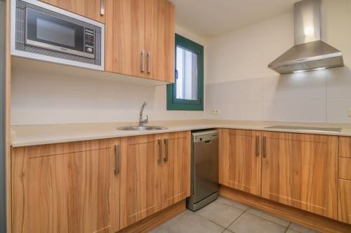 Modern kitchen with wooden cabinets, stainless steel appliances, and white countertops at Rural Montseny apartment in Gualba