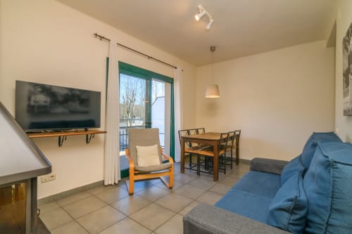 Modern apartment living room in Rural Montseny with TV, dining table, blue sofa, and balcony views of mountains in Gualba.