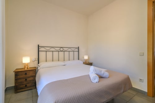 Bedroom in Rural Montseny apartment with metal headboard, wooden nightstand, white bedding, rolled towels, and warm lighting