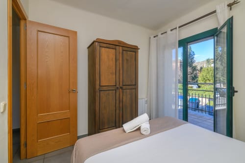 Spacious bedroom in Rural Montseny apartment with wooden furniture, balcony overlooking Gualba mountains, and modern