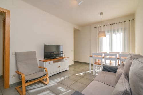 Bright living room in Rural Montseny apartment with sofa, TV, dining table, and mountain views through windows