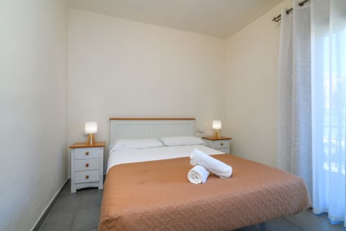 Bright bedroom in Rural Montseny apartment with queen bed, white bedding, wooden nightstands, and mountain views through