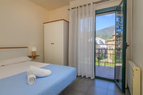 Bright bedroom with blue bedspread, balcony overlooking Montseny mountains, wardrobe, and mountain views at Rural Montseny