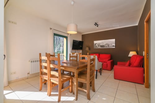 Open-plan living and dining area at Rural Montseny cottage with wooden table, red sofas, and mountain views